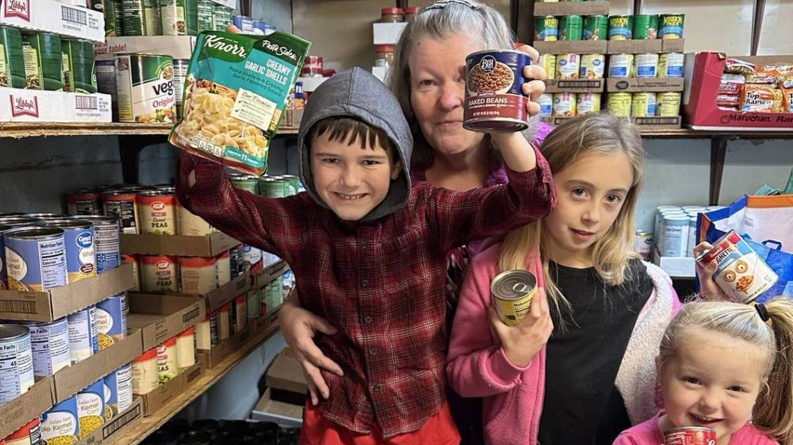 Children and a woman holding up cans of food at the Woodland Food Pantry.
