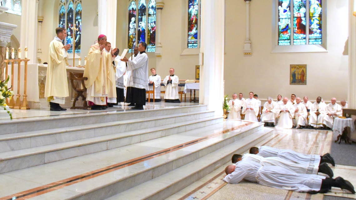 Bishop Ruggieri prays while the three lie prostrate.