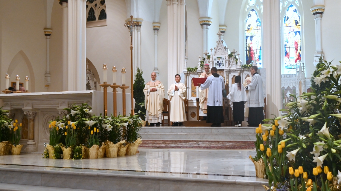 Bishop Ruggieri, Father Seamus Griesbach, altar servers, with flowers in the foreground.