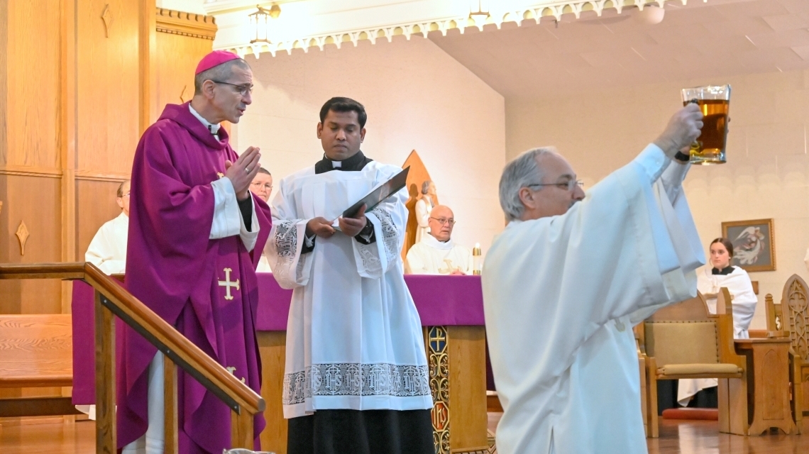 Deacon Rodney Dechaine holds up oil with Bishop James Ruggieri behind him.