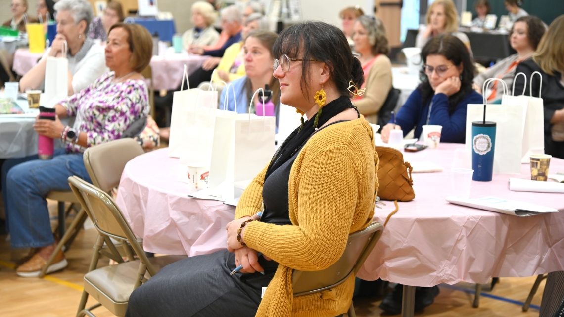 Woman wearing a gold sweater sitting at a table.