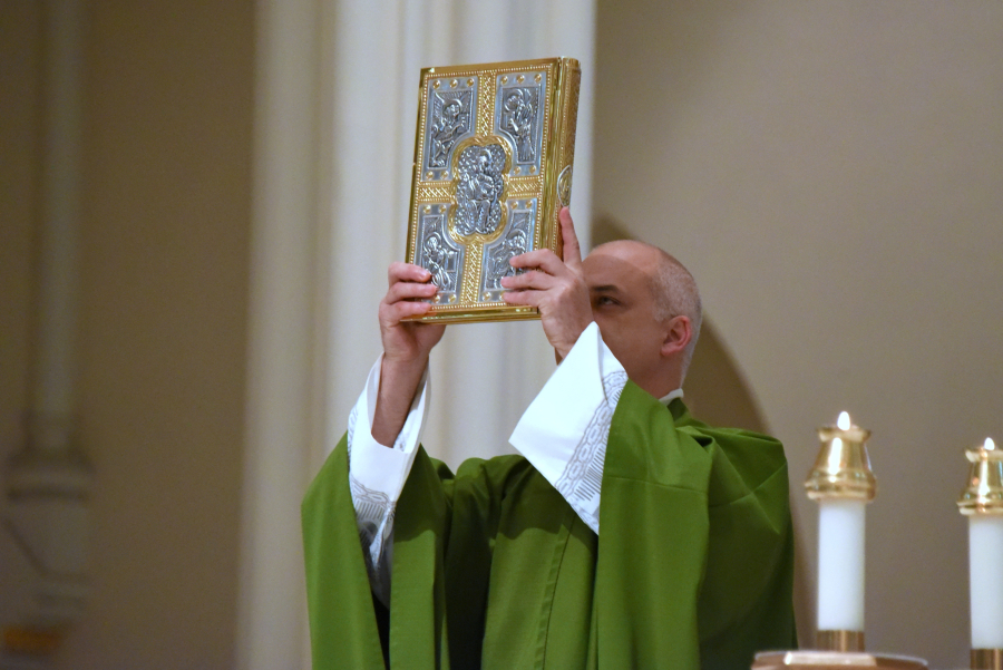 Father Seamus Griesbach holds up the Book of the Gospels.