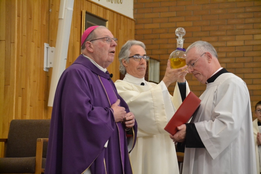 Deacon Carl Gallagher holds up a jar of oil next to Bishop Deeley and Msgr. Marc Caron.