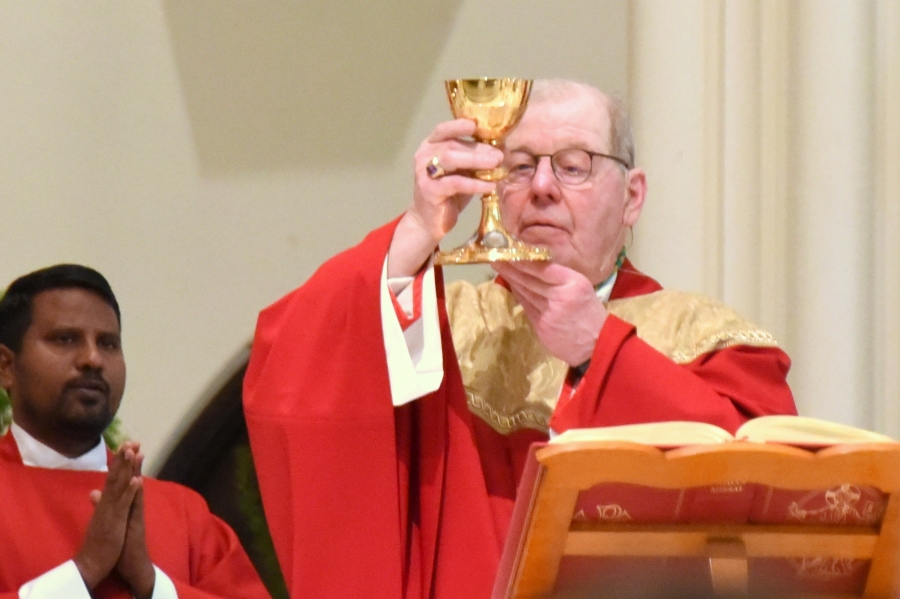 Bishop Deeley wearing red vestments holding up a chalice.