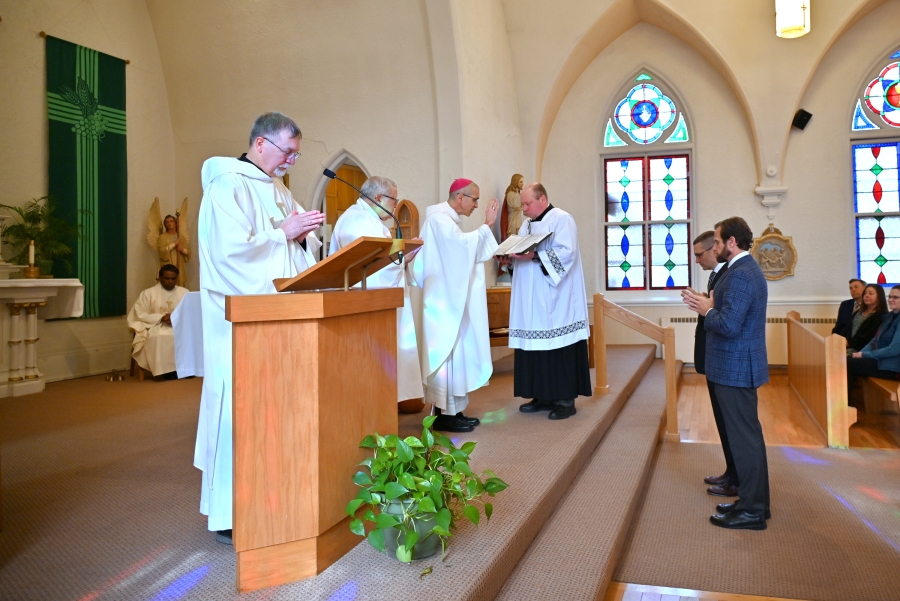 Stephen Ritchie and Richard Roussel stand before the bishop, with Deacon Peter Bernier at the ambo.