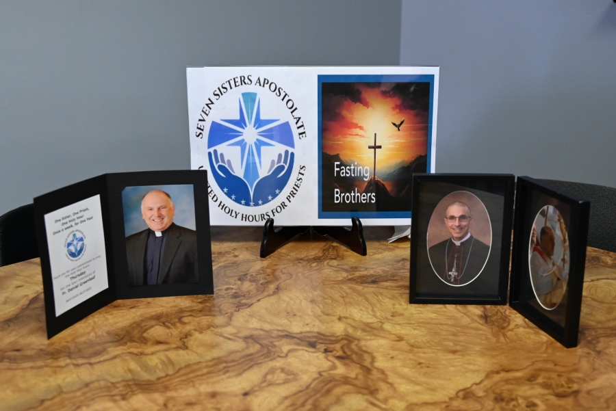 Display showing logos of the Seven Sisters Apostolate and the Fasting Brothers and photos of Father Daniel Greenleaf and Bishop James Ruggieri.