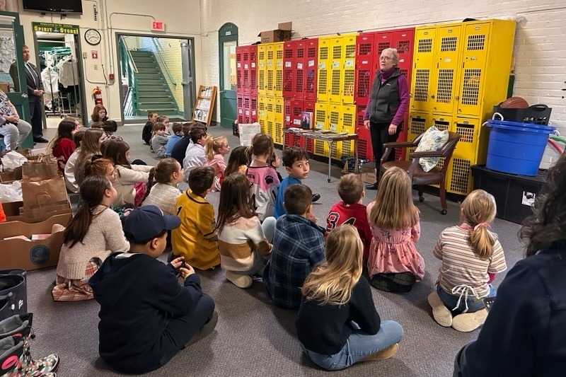 St. John School students sit on the floor listening to a presenter.