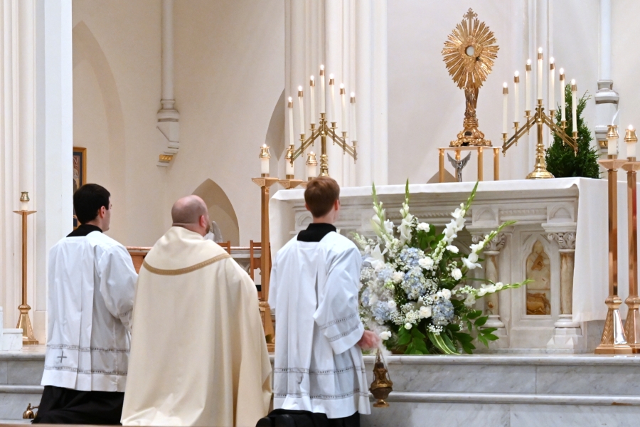 Father Brad Morin and altar servers kneel before the Blessed Sacrament.