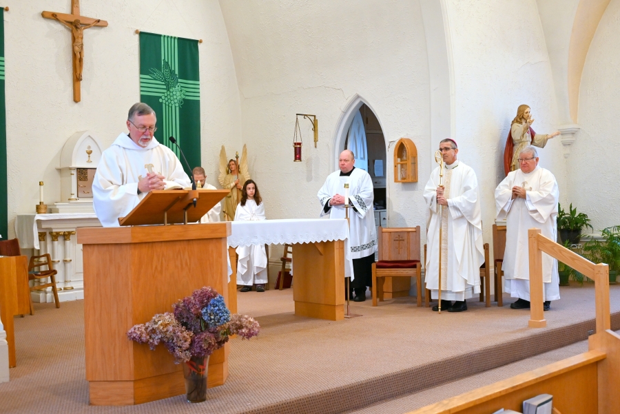 Deacon Peter Bernier reads the Gospel with Bishop Ruggieri and priests in the background.