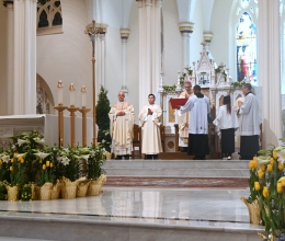 Bishop Ruggieri, Father Seamus Griesbach, altar servers, with flowers in the foreground.