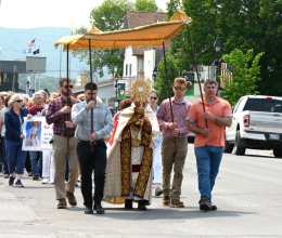 Father Antony Alexander Maria Doss carries a monstrance holding the Blessed Sacrament. Four men carry a canopy which he is walking beneath.