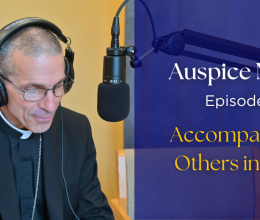 Bishop Ruggieri sitting in front of a microphone. text: "Auspice Maria, Episode 8, Accompanying others in faith"