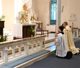 Bishop Ruggieri and altar servers kneel before the altar and the Blessed Sacrament.
