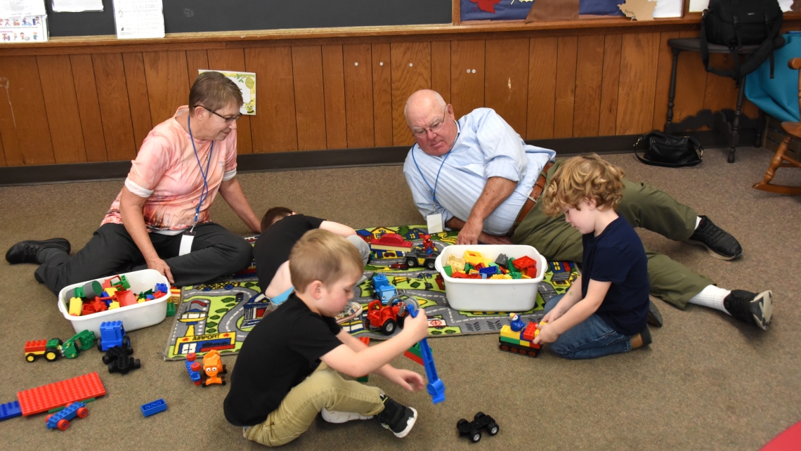 Foster grandparents playing on the floor with three preschoolers.