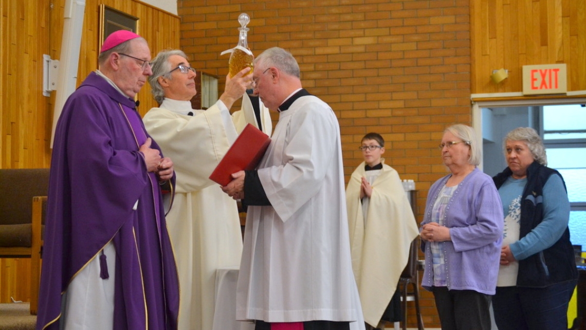 Bishop Robert Deeley next to Deacon Carl Gallagher who is holding up a jar of oil.