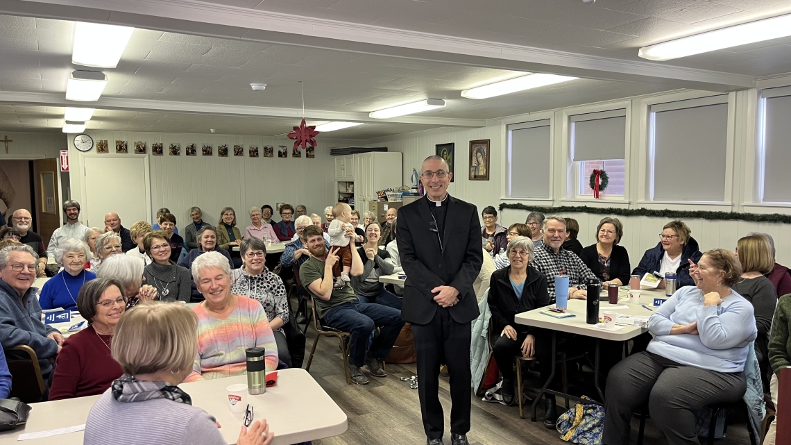 Bishop standing in the center of room surrounded by people seated.