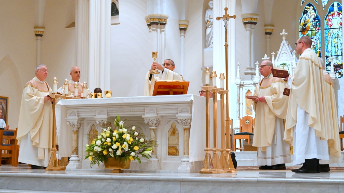 Bishop James Ruggieri holds up the chalice, surrounded by other priests.