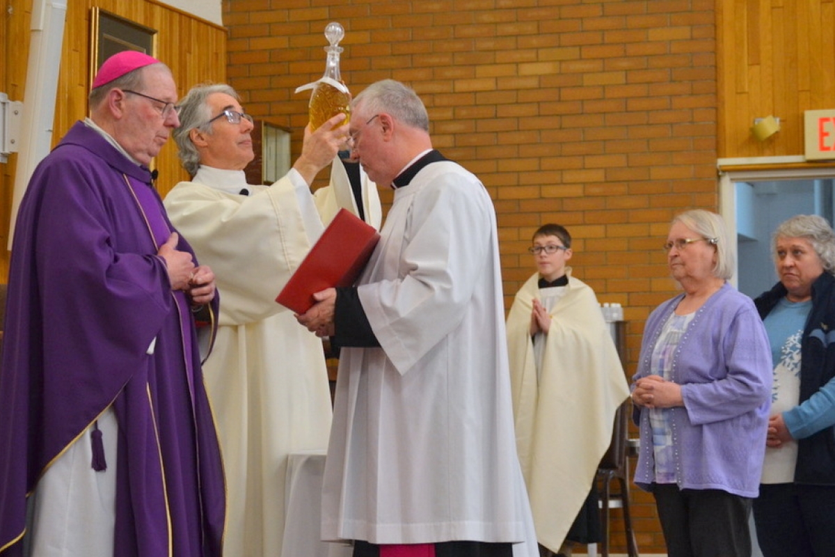 Bishop Robert Deeley next to Deacon Carl Gallagher who is holding up a jar of oil.