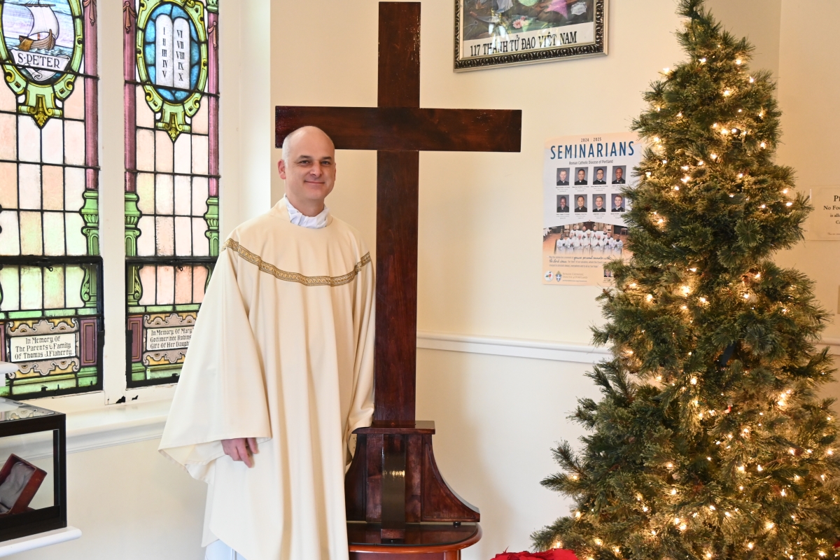 Father Seamus Griesbach standing next to a cross. A Christmas tree is in the corner.