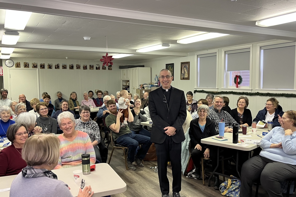 Bishop standing in the center of room surrounded by people seated.