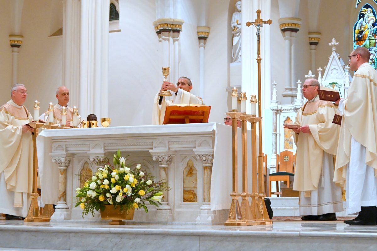 Bishop James Ruggieri holds up the chalice, surrounded by other priests.