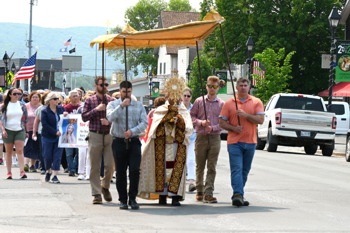 Father Antony Alexander Maria Doss carries a monstrance holding the Blessed Sacrament. Four men carry a canopy which he is walking beneath.